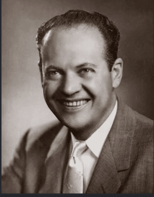 Studio portrait of Leo M. Bernstein, a smiling man in a light suit and patterned tie, photographed against a plain backdrop.